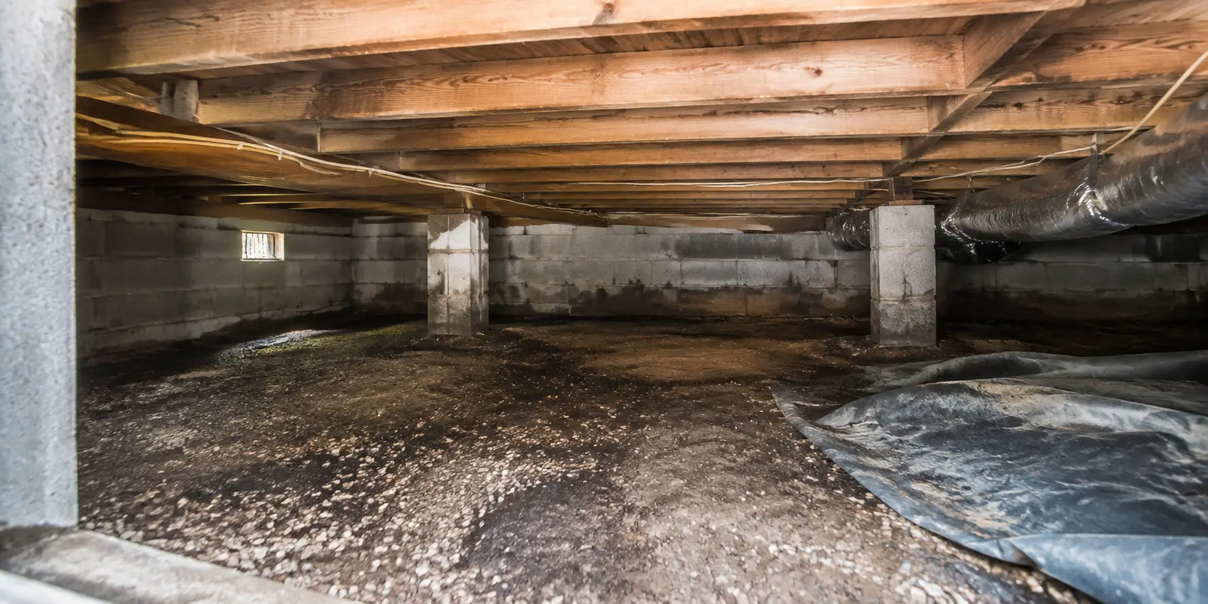 Unfinished crawl space with exposed floor joists, ductwork, support columns, wiring, and a damaged ground vapor barrier.